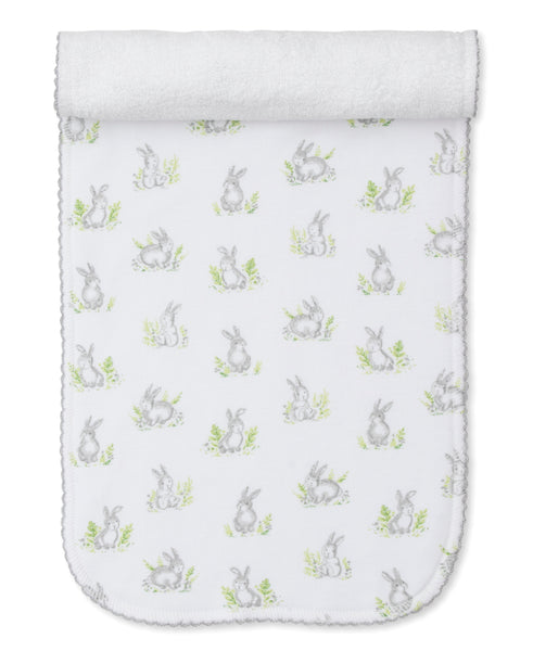 White Kissy Kissy Cottontail Hollows Burp Cloth made from absorbent terry cloth, featuring a pattern of gray rabbits and green leaves with a textured border and a folded top edge.