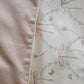 A close-up of Gooselings' Bows & Butterfly Kisses Toddler Duvet shows solid light pink fabric paired with white featuring a delicate bow, floral, and butterfly pattern—ideal for a lightweight toddler duvet.