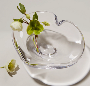 The Simon Pearce Romance Heart Dish features a unique heart-shaped design holding a green and white flower with leaves and buds, plus a matching flower beside it—ideal as romantic table decor or an elegant jewelry holder.
