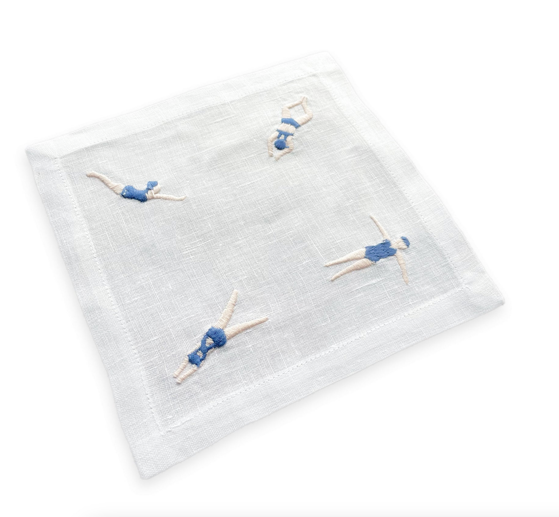 The Freestyle Swim Coaster Set by Haute Home features white linen coasters with four embroidered figures in blue swimsuits, each in a unique swimming pose—perfect for elevating any handcrafted tableware collection.