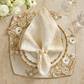A formal spring table features a Kim Seybert Bramble Placemat in Ivory/Natural, white plates, a gold-rimmed napkin ring with a folded napkin, and a bouquet of white flowers alongside elegant glassware.