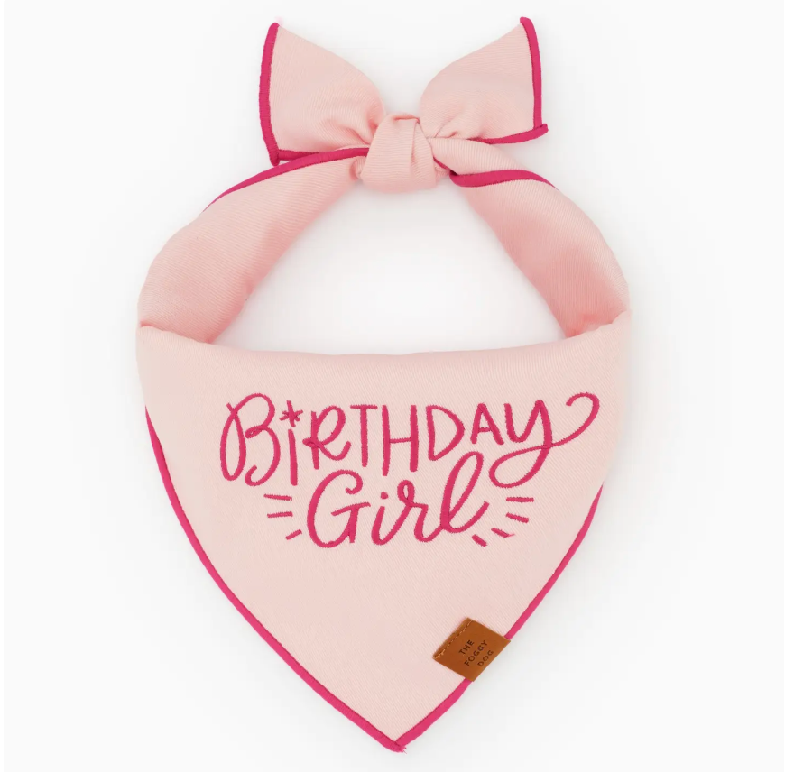 The Foggy Dog Birthday Girl Embroidered Dog Bandana features a light pink fabric, dark pink trim, and a bow, with “Birthday Girl” elegantly embroidered in cursive on the front. This personalized accessory includes a small brown tag at the bottom corner, making it the perfect custom pet bandana for your pup’s special day.