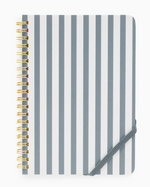 The Sugar Paper Mini Spiral Notebook showcases vertical gray and white stripes, elegant gold coil binding, and is secured with a gray elastic band at the bottom right corner. With lined pages inside, it’s perfect for jotting down your daily to-do lists.