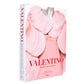 A hardcover book titled “Valentino: Themes & Variations” by Rizzoli, featuring a striking cover image of a model in a pink sculptural dress that embodies the elegance of Valentino’s haute couture collections.