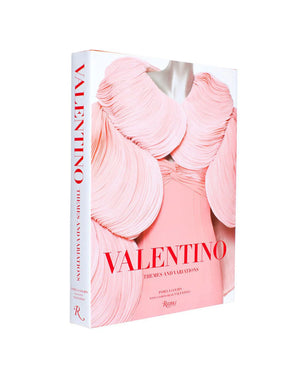 A hardcover book titled “Valentino: Themes & Variations” by Rizzoli, featuring a striking cover image of a model in a pink sculptural dress that embodies the elegance of Valentino’s haute couture collections.