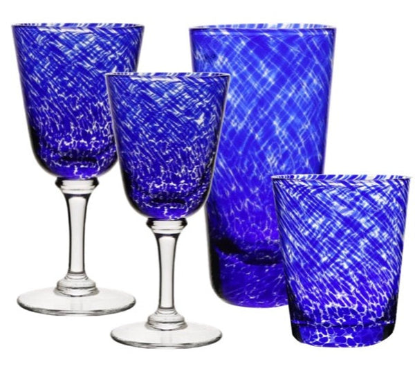 Four cobalt blue, colored glass drinking vessels from William Yeoward Vanessa Blue Collection: two stemmed goblets and two tumblers, isolated on a white background.