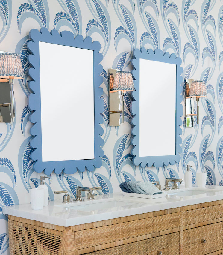A bathroom features two sinks, two Fleur Home Garden District Coquette Rectangle Mirrors in Denim Wash, wall sconces, and patterned blue wallpaper with feather-like designs inspired by Queen Anne fishtail shingles.