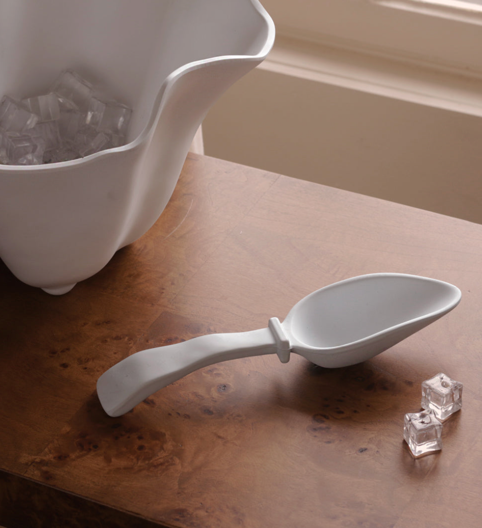 A Beatriz Ball Vida Nube Ice Scoop sits on a wooden surface next to two ice cubes and a white ice container. This stylish melamine scoop is dishwasher safe.