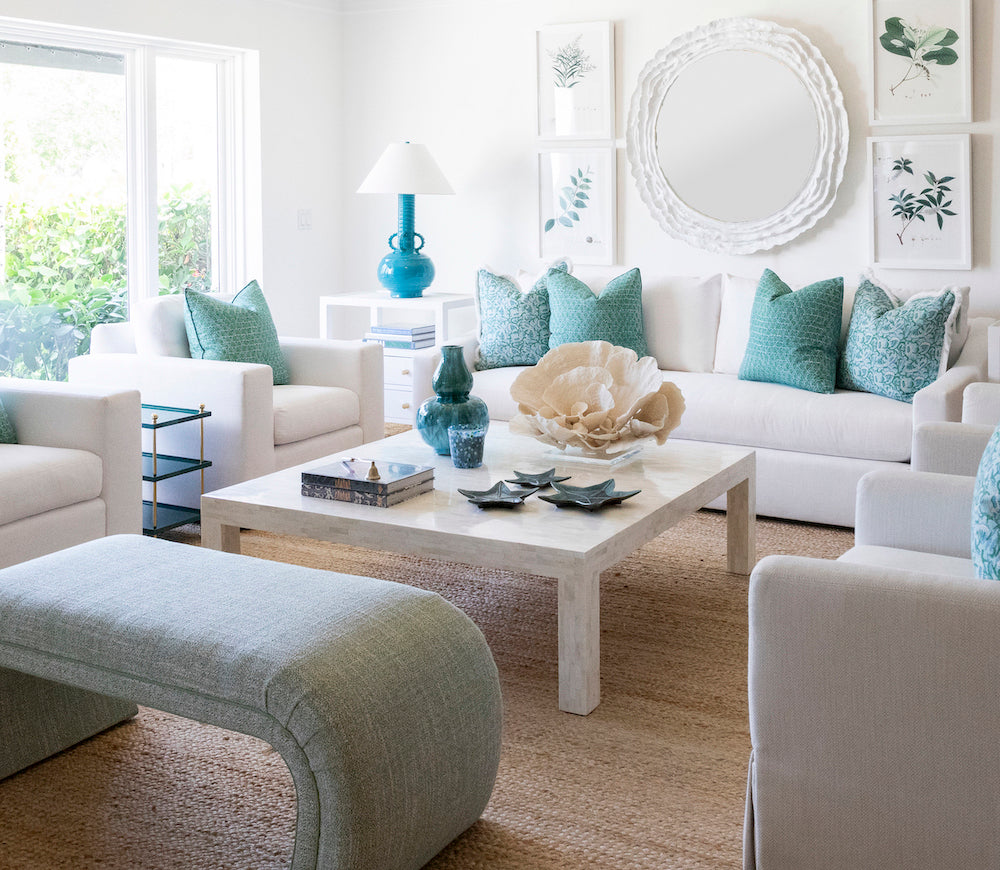Bright living room with white furniture, teal accents, a large round mirror, framed botanical prints, and the Bojay Bone Inlay Cocktail Table featuring elegant bone inlay artistry for a stylish space.