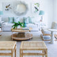 A cozy Sea Cliff living room showcases a Selamat Sea Cliff Slipper Chair in Palmetto Stripe, complemented by a white sofa with blue and white cushions. Rattan wicker furniture, a round mirror, bird-themed art, and a potted plant on the round coffee table complete the setting.
