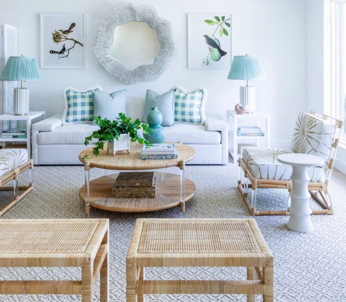 A cozy Sea Cliff living room showcases a Selamat Sea Cliff Slipper Chair in Palmetto Stripe, complemented by a white sofa with blue and white cushions. Rattan wicker furniture, a round mirror, bird-themed art, and a potted plant on the round coffee table complete the setting.