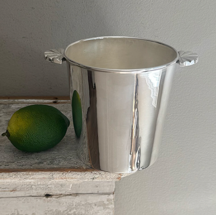 A Vintage Ice Bucket with Shell Handles from Hôtel Silver sits on a wooden surface next to a whole green lime.