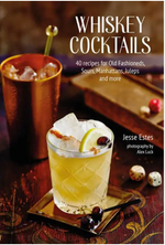 A glass of whiskey cocktail with ice and garnish rests on a table beside dice and a metal cup. The cover displays the title “Whiskey Cocktails” from Simon & Schuster, inviting readers to explore bourbon-based drinks and creative recipes featured in this expertly crafted recipe book.