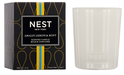 The Nest Amalfi Lemon & Mint Collection candle comes in a white jar with packaging inspired by the Amalfi Coast, featuring a black box adorned with yellow and blue accents.