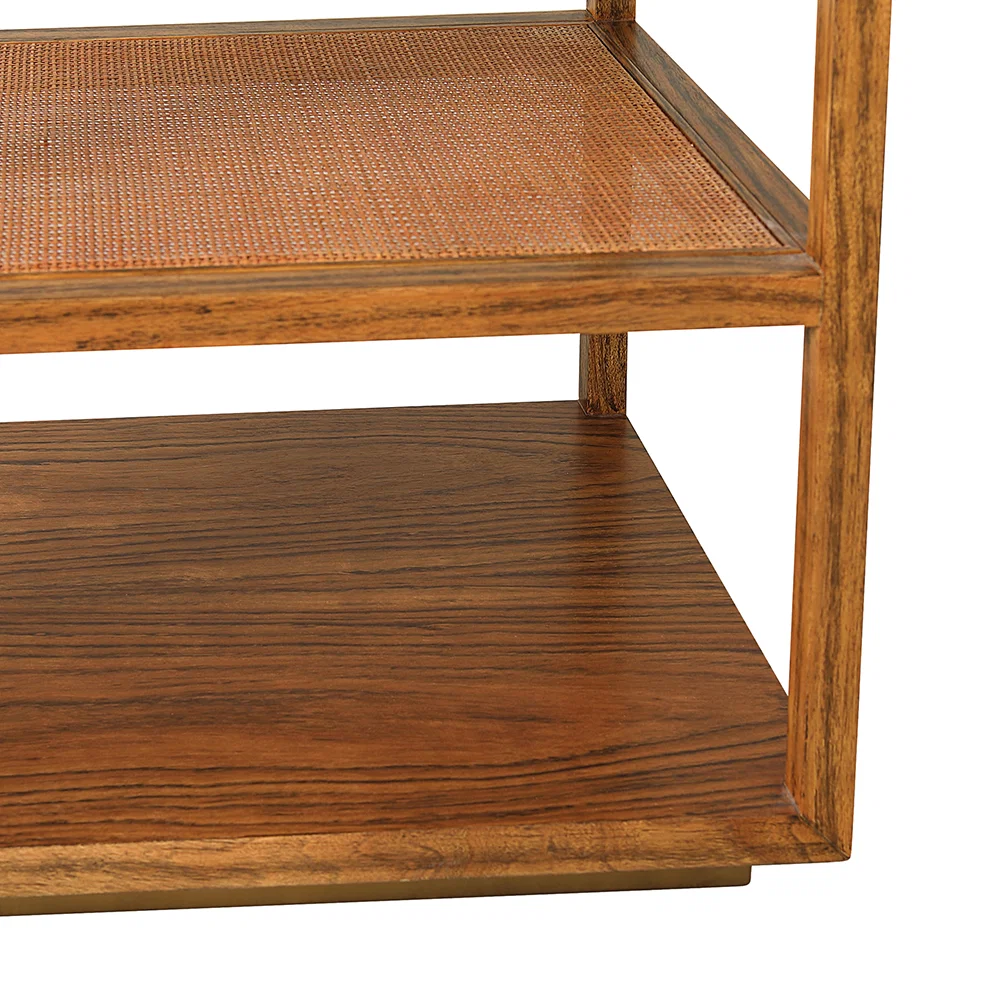 The Orca Side Table by Julian Chichester showcases two wooden shelves—an upper shelf with an antiqued rattan surface and a lower shelf finished in smooth wood grain—all elegantly supported by an aged brass base inspired by refined African Walnut furniture.
