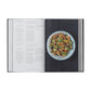 Japan: The Cookbook by Phaidon is open to a recipe on the left and a bowl of stir-fried vegetables on the right, all set against a dark textured background.