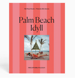A 750-piece puzzle from the Piecework Slim Aarons Puzzle Collection features the “Palm Beach Idyll” photo of people relaxing under a canopy on a beach with palm trees, set against a pink and red striped background, and is printed on high-quality art paper for vibrant colors and durability.