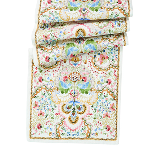 The Sofia Table Runner by Juliska is a folded, rectangular linen runner featuring intricate floral and geometric patterns in pastel pink, blue, green, and gold on white—ideal for spring table decor.