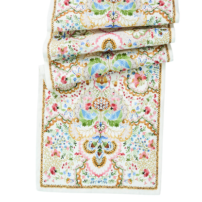 The Sofia Table Runner by Juliska is a folded, rectangular linen runner featuring intricate floral and geometric patterns in pastel pink, blue, green, and gold on white—ideal for spring table decor.