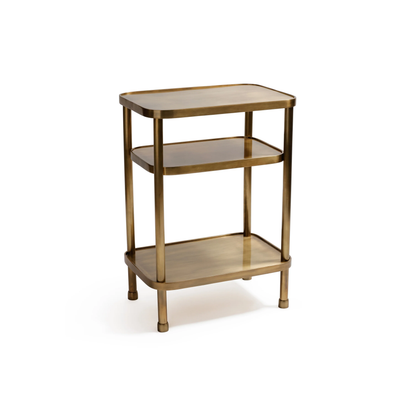 The Aman Etagere by Zodax is a compact, three-tiered brass side table with rounded edges and four legs, offering minimalist style inspired by an Etagere—perfect for display against a white backdrop.