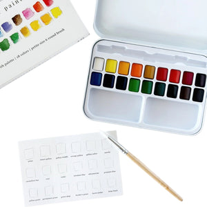 The Emily Lex Studio Watercolor Paint Set includes 18 watercolor paints in a metal tin, a color chart card, and a paintbrush, all thoughtfully arranged on a white surface—making it the ideal travel kit for painting on the go.