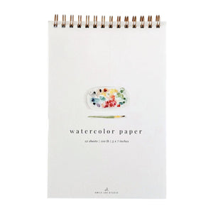 Emily Lex Studio Spiral Watercolor Paper Pad featuring an illustrated paint palette and brush on the cover, labeled “watercolor paper 12 sheets | 110 lb | 5 x 7 inches.”.