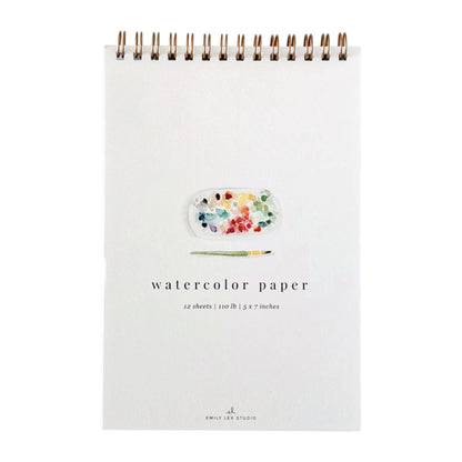 Emily Lex Studio Spiral Watercolor Paper Pad featuring an illustrated paint palette and brush on the cover, labeled “watercolor paper 12 sheets | 110 lb | 5 x 7 inches.”.