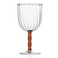 The Rivoli Drinkware and Tealight Collection by Ichendorf Milano features a clear ribbed glass goblet with a wavy rim, short amber stem, and round base—an elegant example of hand-crafted glassware.