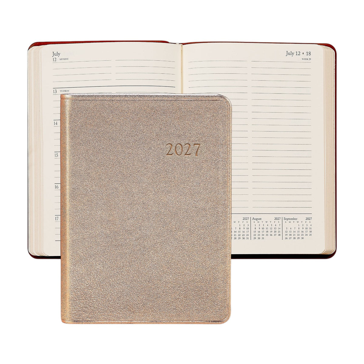 The image features a closed 2027 Weekly Notebook by Graphic Image in gold, positioned in front of an open planner displaying a week in July. Both planners have lined pages, calendar layouts, and distinctive red-edged covers—ideal for use as an appointment book or a stylish leather notebook.