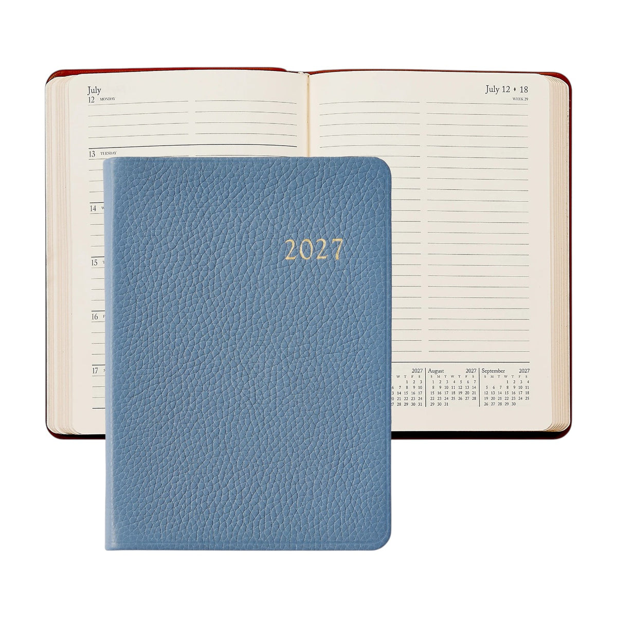 A closed Graphic Image 2027 Weekly Notebook in blue is placed on top of an open appointment book displaying the week of July 12–18, with mini monthly calendars at the bottom of the right page.