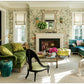 An inviting living room adorned with floral wallpaper, green and blue sofas, a fireplace, large mirror, coffee table, and multiple windows dressed in Roman shades—showcasing the neo-traditionalist interior design principles featured in *The Well-Loved House* by Penguin Random House.
