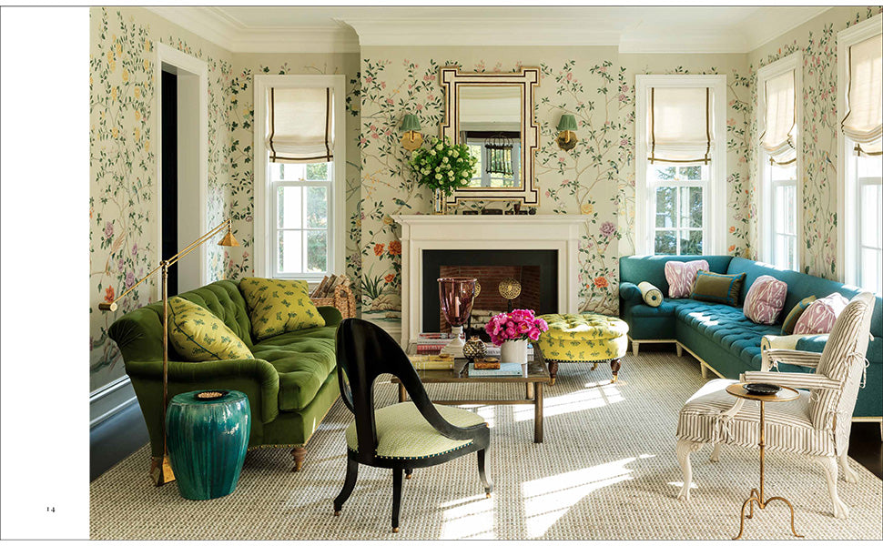 An inviting living room adorned with floral wallpaper, green and blue sofas, a fireplace, large mirror, coffee table, and multiple windows dressed in Roman shades—showcasing the neo-traditionalist interior design principles featured in *The Well-Loved House* by Penguin Random House.