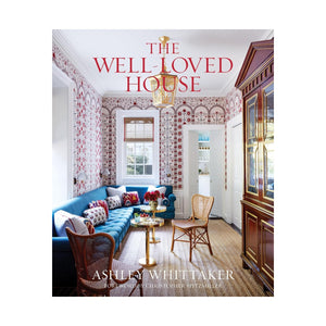 Book cover of The Well-Loved House from Penguin Random House, showcasing a vibrant, traditional living room with patterned wallpaper and a blue sofa—a perfect representation of the neo-traditionalist interior design style that defines Ashley Whittaker’s work.