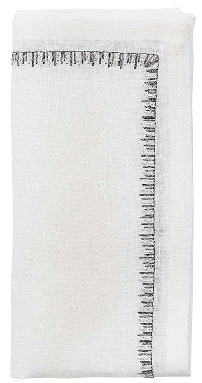 The Filament Napkin Set by Kim Seybert features crisp white linen napkins, elegantly folded and accented with decorative black embroidered stitching along two edges.