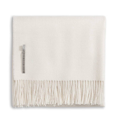 The Alicia Adams Alpaca Classic Throw Collection features a cream-colored baby alpaca blanket, fair-trade made in Peru, neatly folded with fringed edges and a small fabric label.
