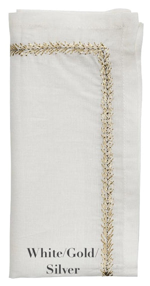 A folded white linen napkin from the Kim Seybert Jardin Napkin Set features gold and silver embroidery along the border, labeled "White/Gold/Silver" at the bottom.