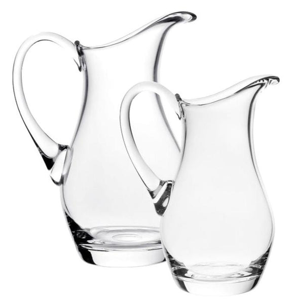 Two elegant William Yeoward Crystal Whitney pitchers, featuring curved spouts and handles, stand side by side on a plain background—ideal as a stunning wedding gift.