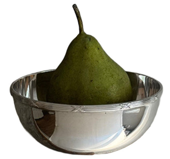 A green pear rests in a Hôtel Silver Vintage Bowl with Ribbon & Reed Top Rim, its reflection shimmering on the polished silver surface.