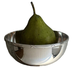 A green pear rests in a Hôtel Silver Vintage Bowl with Ribbon & Reed Top Rim, its reflection shimmering on the polished silver surface.