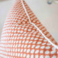 Close-up of the Associated Design Mandarin Wicker Outdoor Pillow, featuring an orange and white pattern, visible seam, and white piping along the edge, expertly crafted for outdoor elegance.