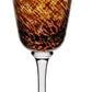 The Vanessa Tortoise Collection wine glass by William Yeoward Crystal features a clear stem and a bowl with a brown, orange, and yellow marbled pattern that creates an elegant optical illusion.