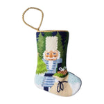 The Bauble Stockings Winter Solstice Nutcracker Needle Point Stocking features a hand-stitched nutcracker and toy sack design with a gold hanging loop.