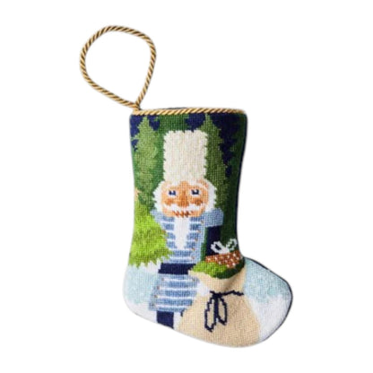 The Bauble Stockings Winter Solstice Nutcracker Needle Point Stocking features a hand-stitched nutcracker and toy sack design with a gold hanging loop.