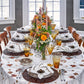 Formal dining table set for a meal with autumn décor, floral centerpieces, orange and yellow candles, glassware on a leaf-patterned cloth, and Kim Seybert Wood Matrix Placemats accented with handcrafted wooden beads.