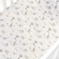 The Gooselings Dino Dreams Bedding Collection features a white crib sheet adorned with illustrated dinosaurs, palm trees, and rocks in soothing neutral tones. Expertly fitted over a crib mattress, this sheet is crafted from breathable fabric for optimal baby comfort and is OEKO-TEX certified for added peace of mind.