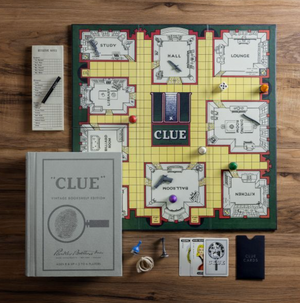A Clue Vintage Bookshelf Edition board game set by WS Game Company on a wooden table, featuring a game board, clue cards, hall, lounge, ballroom, other rooms, tokens, score sheets, a linen-wrapped booklet from the Hasbro editions collection, and dice.