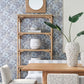 Dining area with a wooden table, upholstered chairs, and the Currey and Company Olisa Etagere displaying decorative vases, a leafy plant, and set against floral-patterned wallpaper. A round mirror hangs above the shelves.