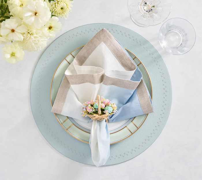 A formal table setting with stacked plates, a Kim Seybert Bloom Napkin Ring in Natural/Multi, faux flowers, wine and water glasses, plus white blooms—perfect for elegant spring gatherings.