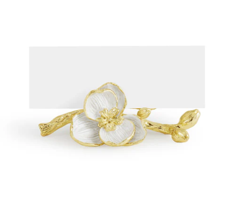 The Michael Aram Orchid Place Card Holder Set features gold and white, handcrafted enamel holders shaped like orchids, adding luxury to your table decor with an elegant blank card behind each decorative bloom.