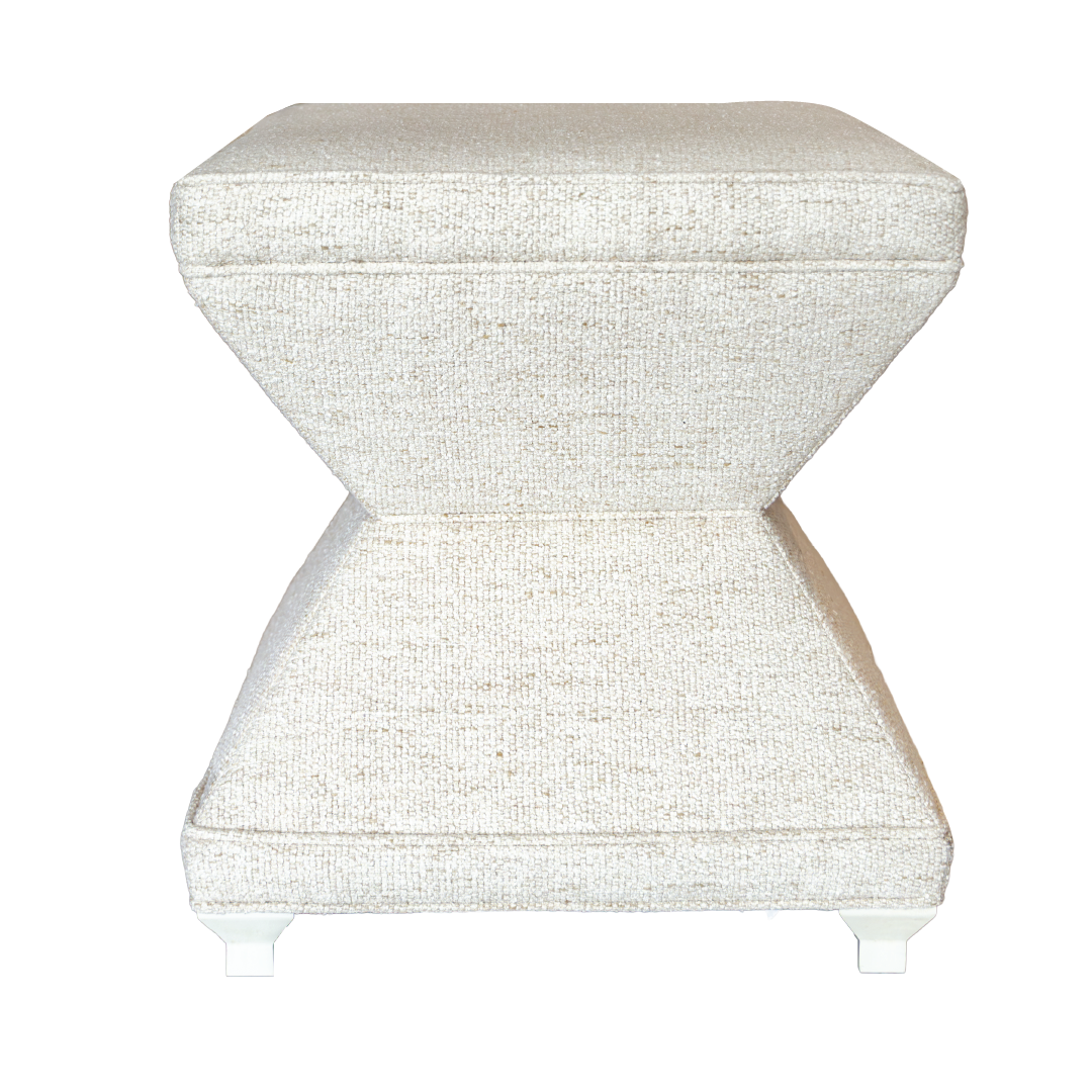 The Serge Ottoman by Hickory Chair is a modern, hourglass-shaped stool upholstered in light beige fabric with short carved maple feet, inspired by the elegance of a French Modernist ottoman and shown against a white background.